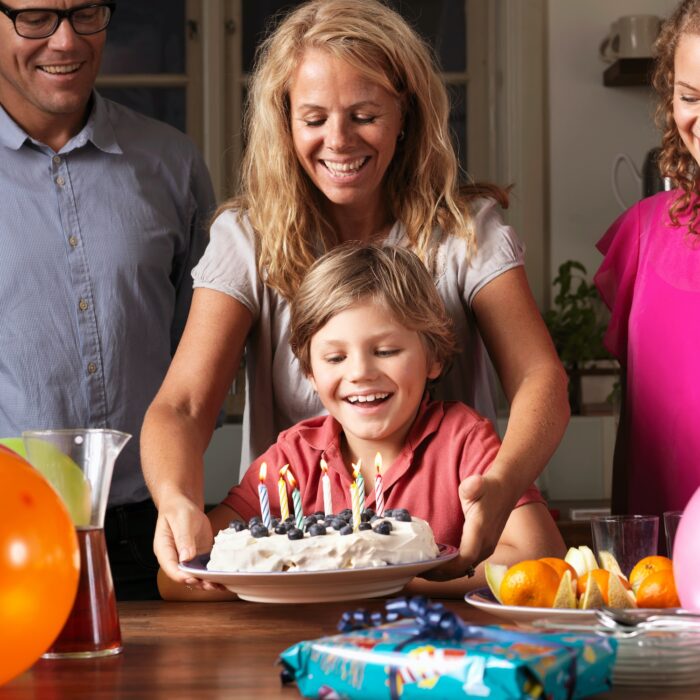 Mother giving boy birthday cake at party